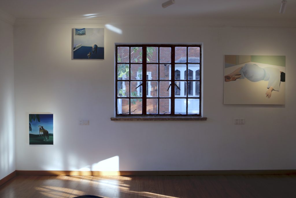 A white wall. 3 paintings hanging on it. In the middle it is a window to look outside. A painting of two dogs on the bottom left. A painting of a man with a dog on the top left. A painting of a female figure in light blue lying on the floor on the right side of the window.