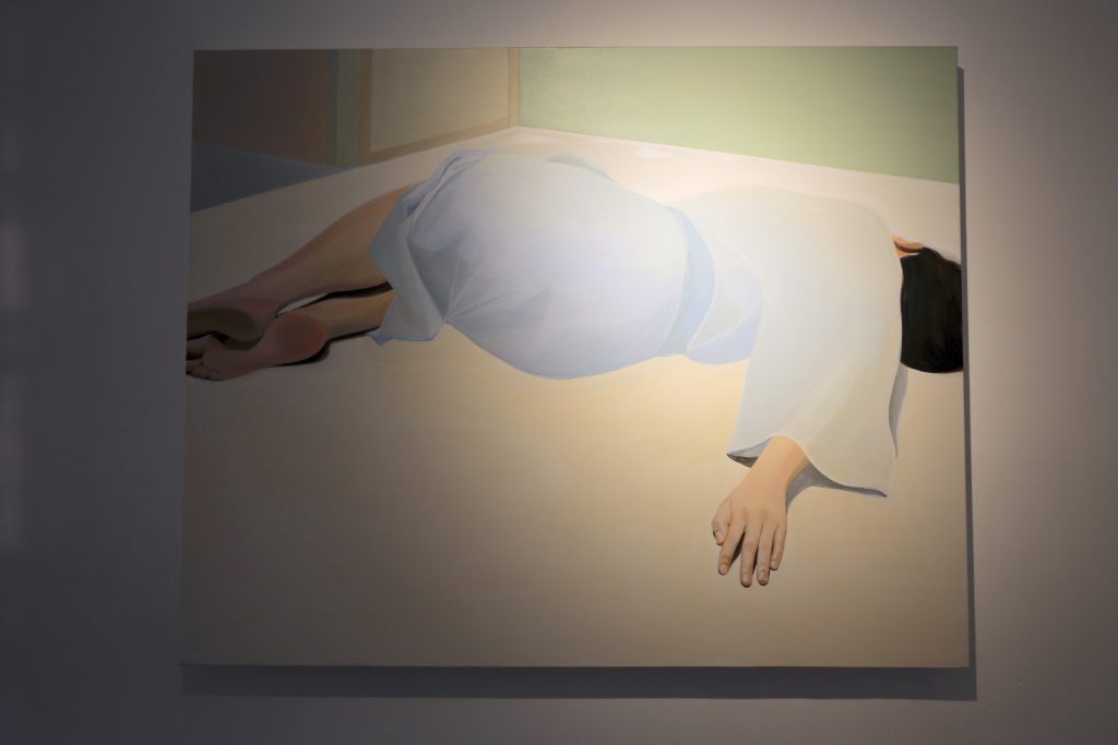 A painting of a female figure in light blue lying on the floor on the right side of the window.