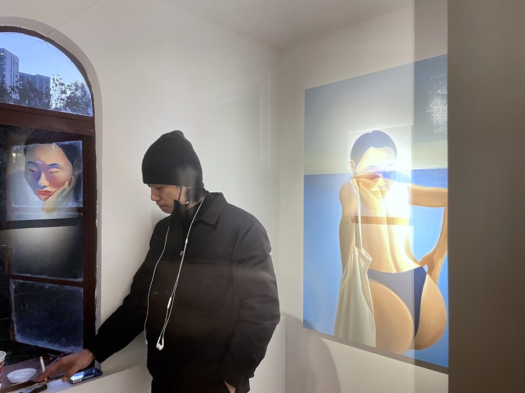 A guy smoking by the side of the window, which has a reflection of the self-portrait of the artist looking into nowhere. On the wall behind the man is a painting of a female figure in swimsuit, with a reflection of the self-portrait.